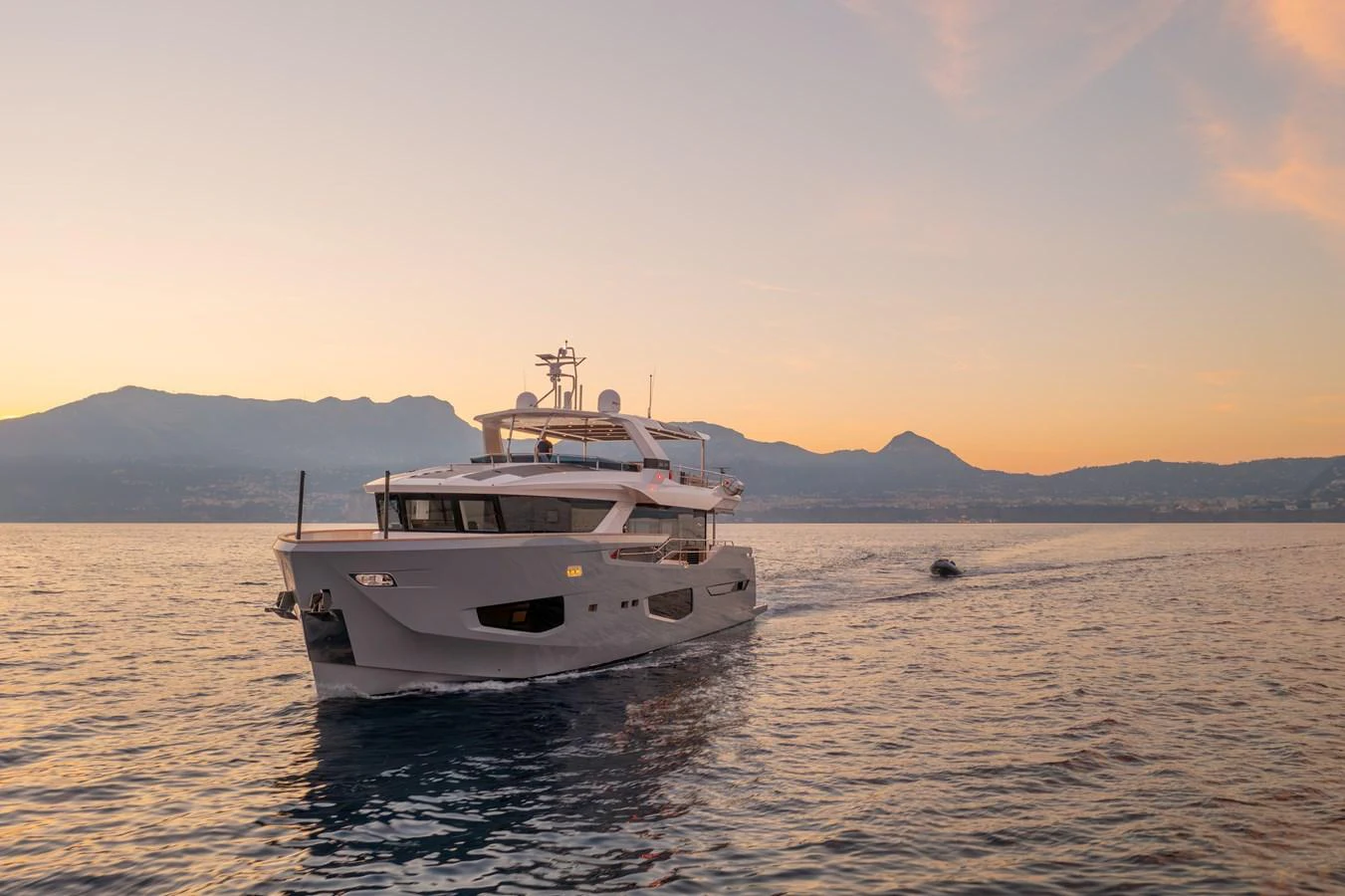 A stunning yacht cruises gracefully on calm waters at sunset, with mountains in the background. aboard KAMOKA Yacht for Sale