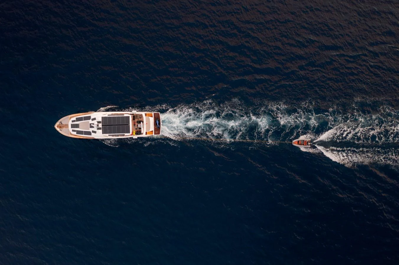 An aerial view of a sleek yacht cruising through deep blue waters with a tender in tow. aboard KAMOKA Yacht for Sale