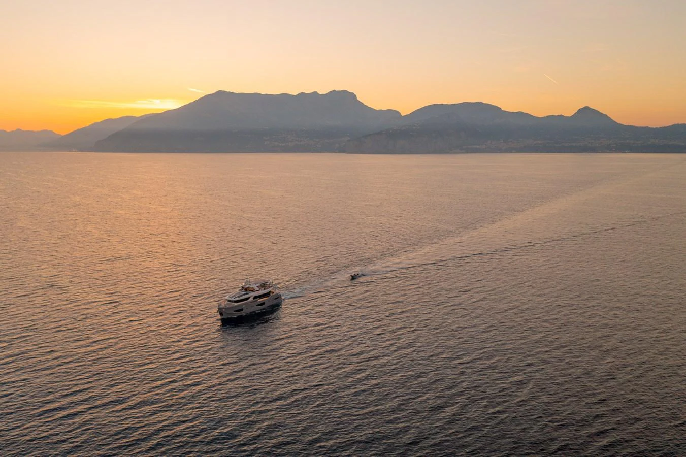A luxurious yacht cruises serenely at sunset with a tender trailing behind. aboard KAMOKA Yacht for Sale