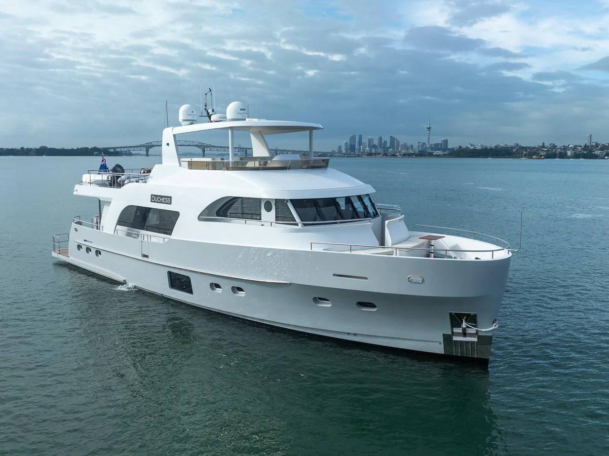 A sleek white yacht cruises gracefully on calm waters with a city skyline in the background. aboard DUTCHESS Yacht for Sale
