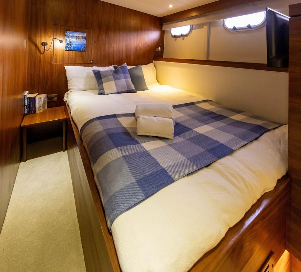 A cozy guest stateroom features a comfortable bed with a blue and white checkered blanket and warm wood paneling. aboard DUTCHESS Yacht for Sale