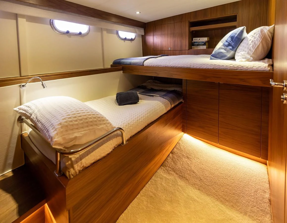 The guest cabin features cozy bunk beds with warm wood finishes and soft lighting. aboard DUTCHESS Yacht for Sale