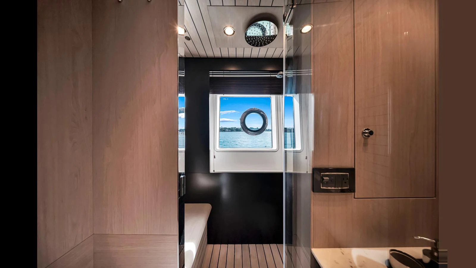A modern yacht bathroom featuring sleek wood paneling and a view of the sea through a porthole window. aboard CLOUD 9 Yacht for Sale