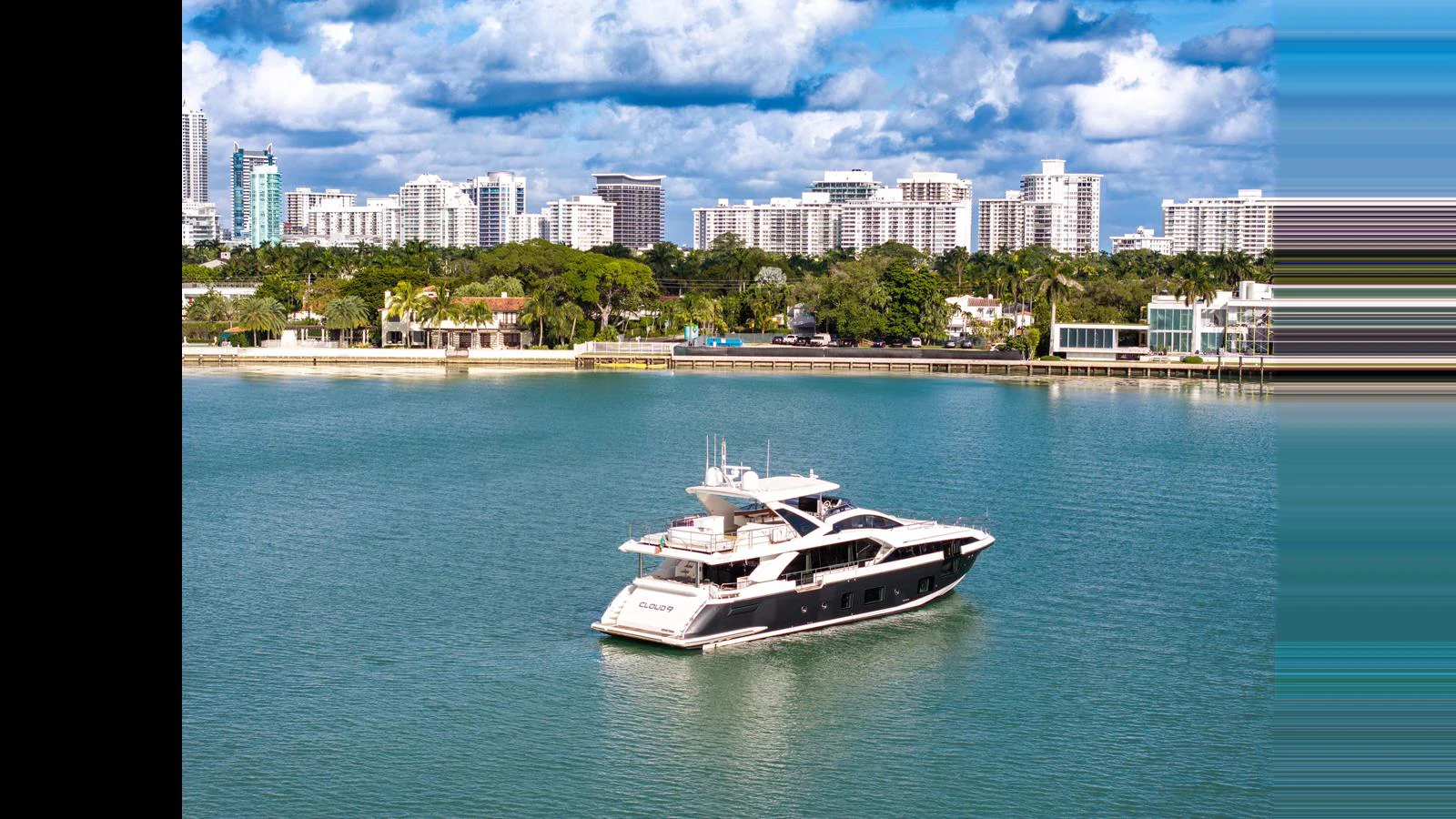 A sleek yacht cruises in a serene harbor with a city skyline in the background. aboard CLOUD 9 Yacht for Sale