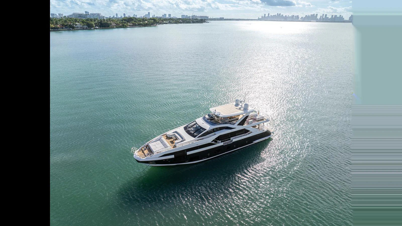 A sleek yacht glides gracefully on calm waters with a cityscape in the background. aboard CLOUD 9 Yacht for Sale