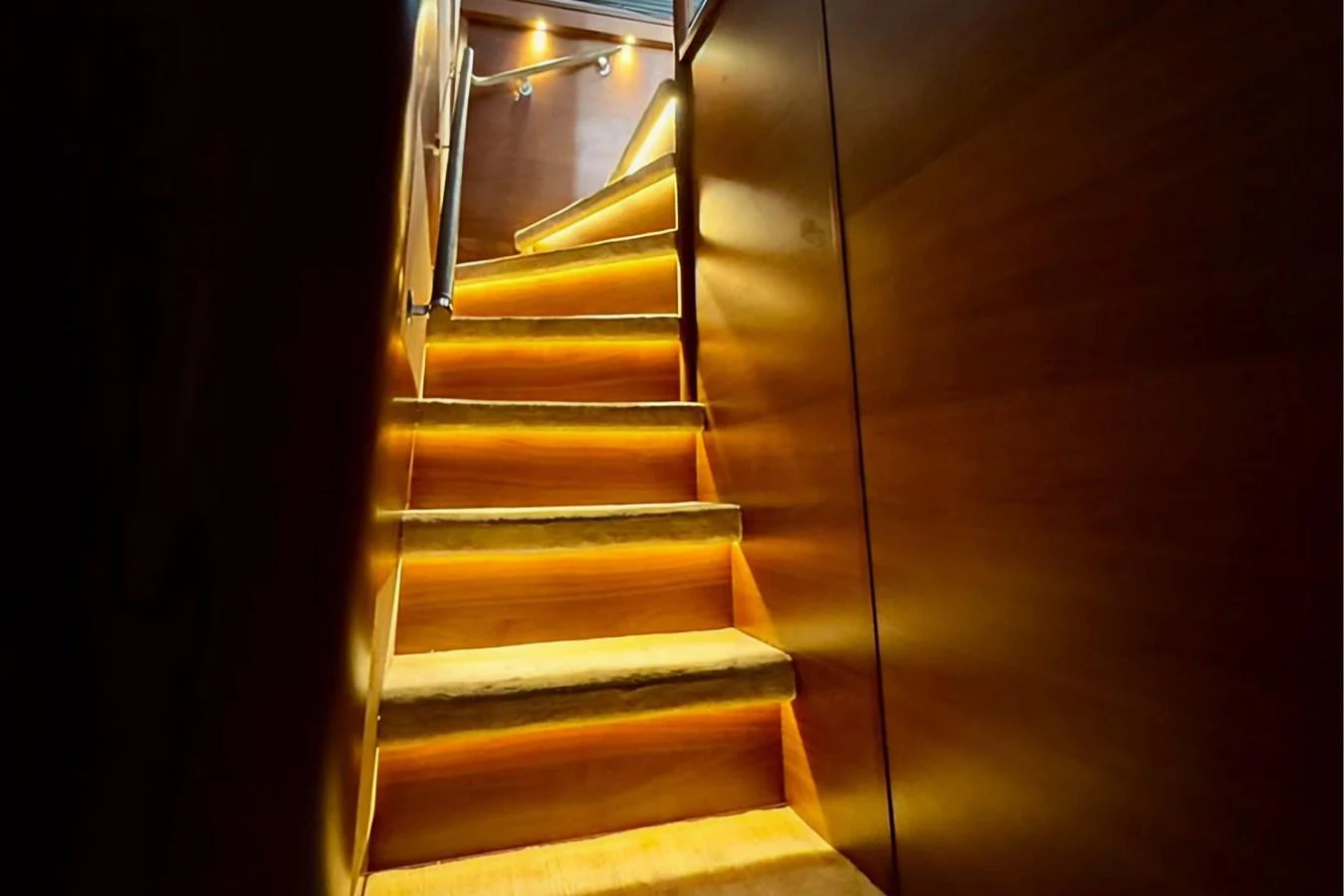 A warmly lit staircase with wooden steps and handrails leads to the upper deck. aboard LADY N Yacht for Sale
