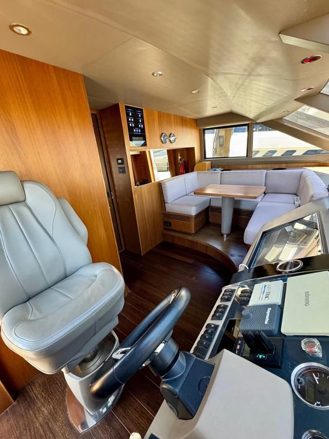 The helm area features a comfortable captain's chair and a well-equipped control panel, with a cozy seating area in the background. aboard LADY N Yacht for Sale