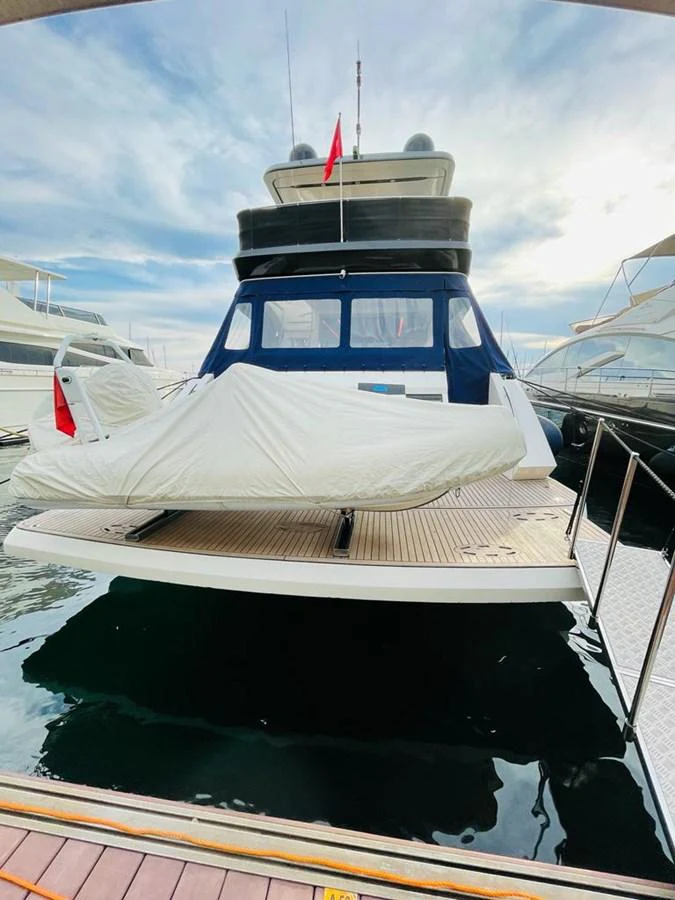 The yacht is docked at the marina, showcasing its sleek stern and covered tender. aboard ASB Yacht for Sale