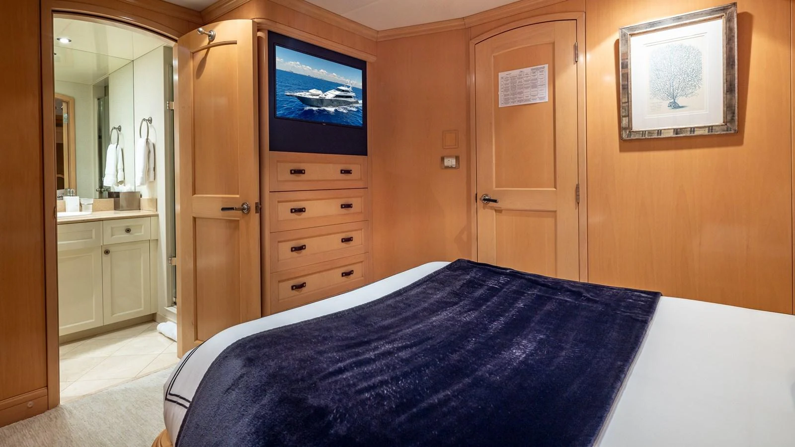 The stateroom features a cozy bed with a navy blanket, wooden cabinetry, and an ensuite bathroom. aboard BAD COMPANY Yacht for Sale