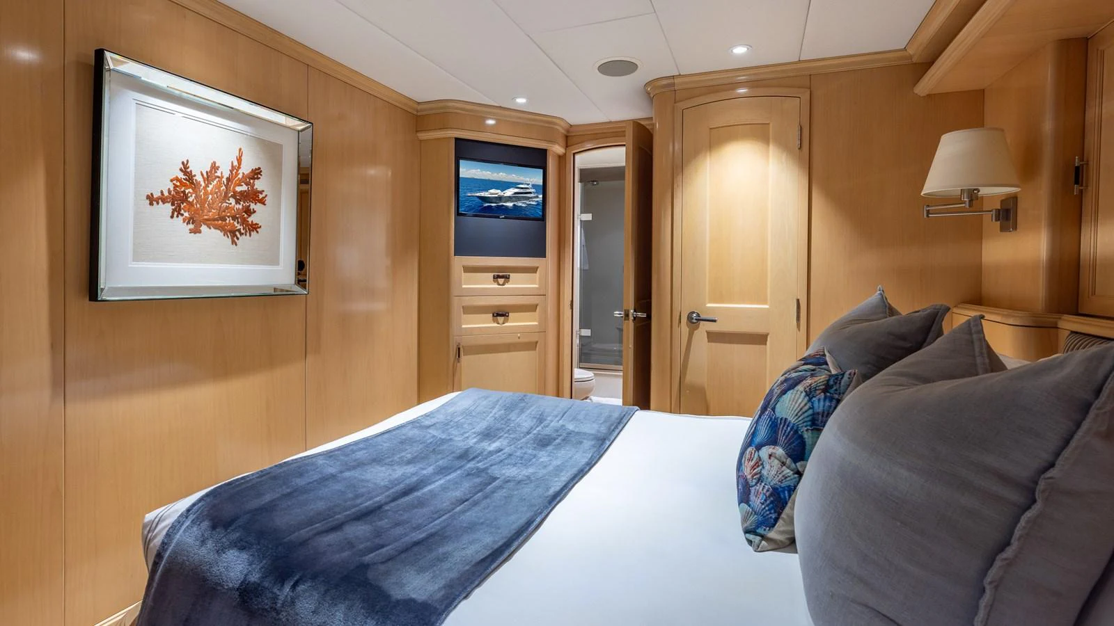 A cozy stateroom with wooden paneling and a comfortable bed adorned with plush pillows and a blue throw blanket. aboard BAD COMPANY Yacht for Sale