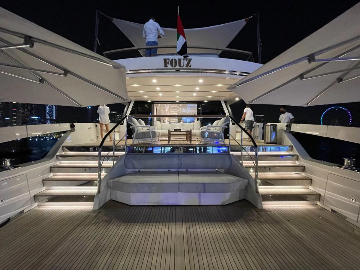 The yacht's aft deck is beautifully illuminated at night, showcasing a luxurious seating area and elegant stairs leading up to the upper deck. aboard FOUZ Yacht for Sale
