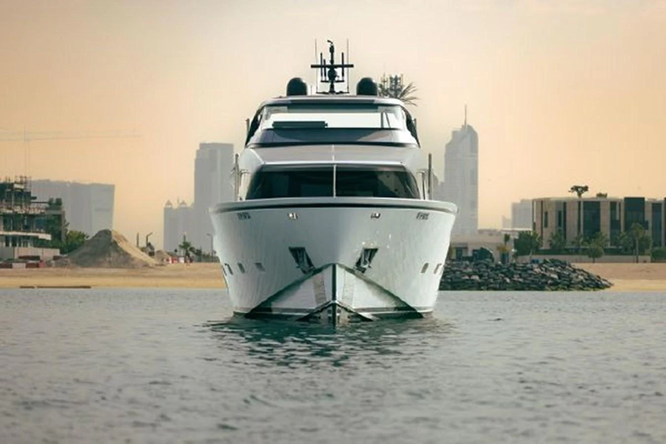 A sleek yacht is seen head-on, floating gracefully on calm waters with a cityscape in the background. aboard FOUZ Yacht for Sale