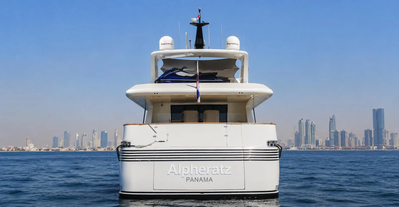A luxurious yacht is seen from the rear with a city skyline in the background. aboard ALPHERATZ Yacht for Sale