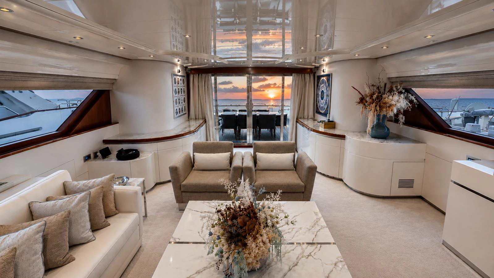 The salon features elegant seating with a stunning view of the sunset through large windows. aboard ALPHERATZ Yacht for Sale