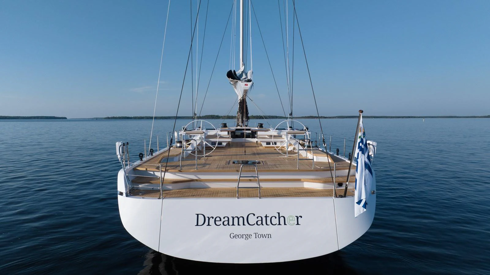 A sleek yacht with a spacious deck is seen from the rear, floating serenely on calm waters. aboard DREAMCATCHER Yacht for Sale