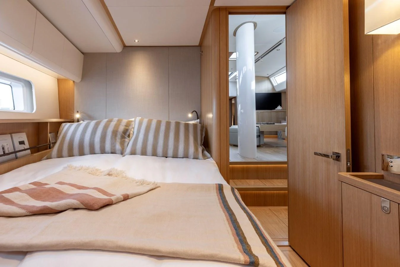 The stateroom features a cozy bed with striped pillows and a blanket, leading to a well-lit corridor. aboard DREAMCATCHER Yacht for Sale