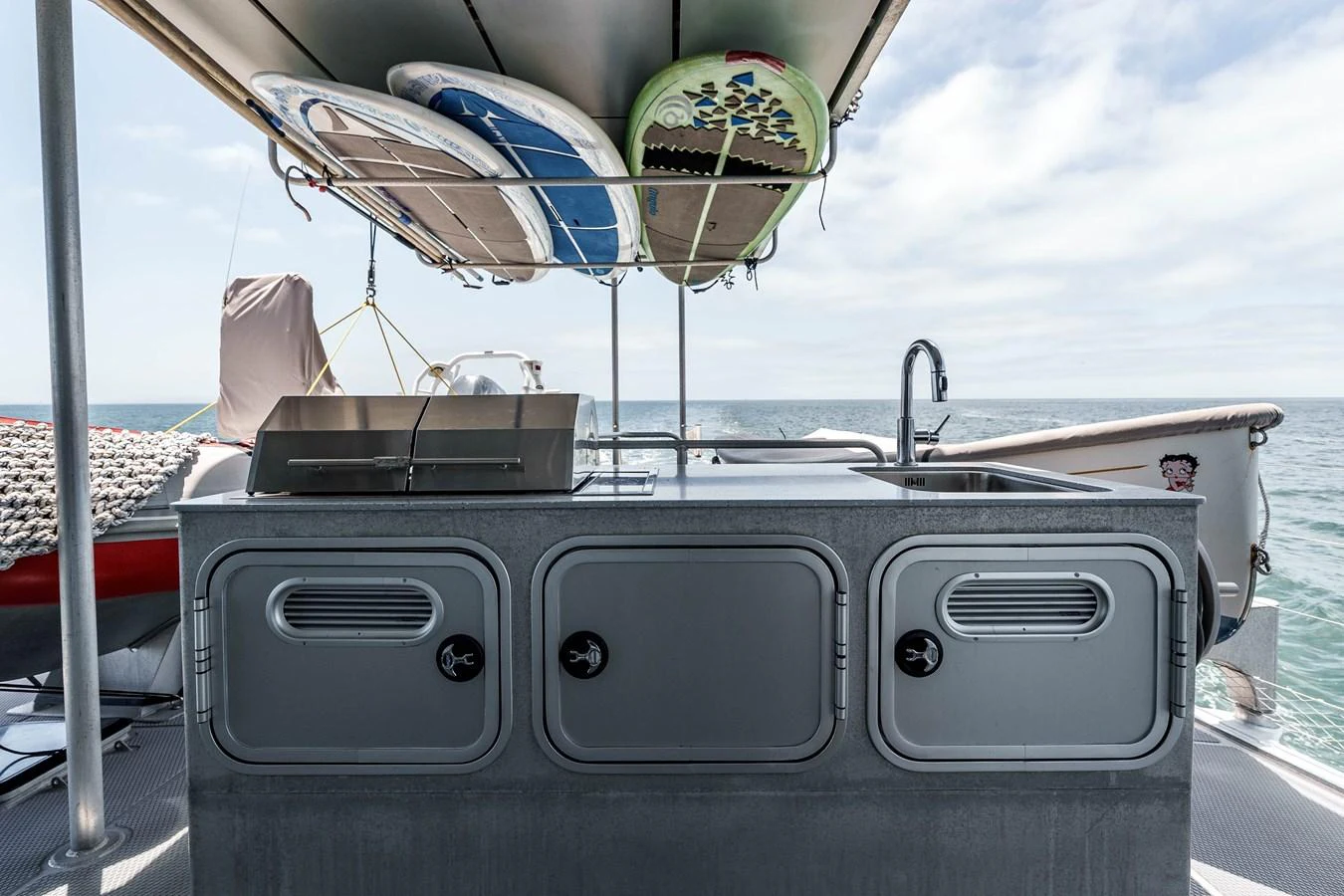 The yacht features a well-equipped outdoor galley with surfboards stored overhead, perfect for enjoying meals by the sea. aboard UGLY BETTY Yacht for Sale