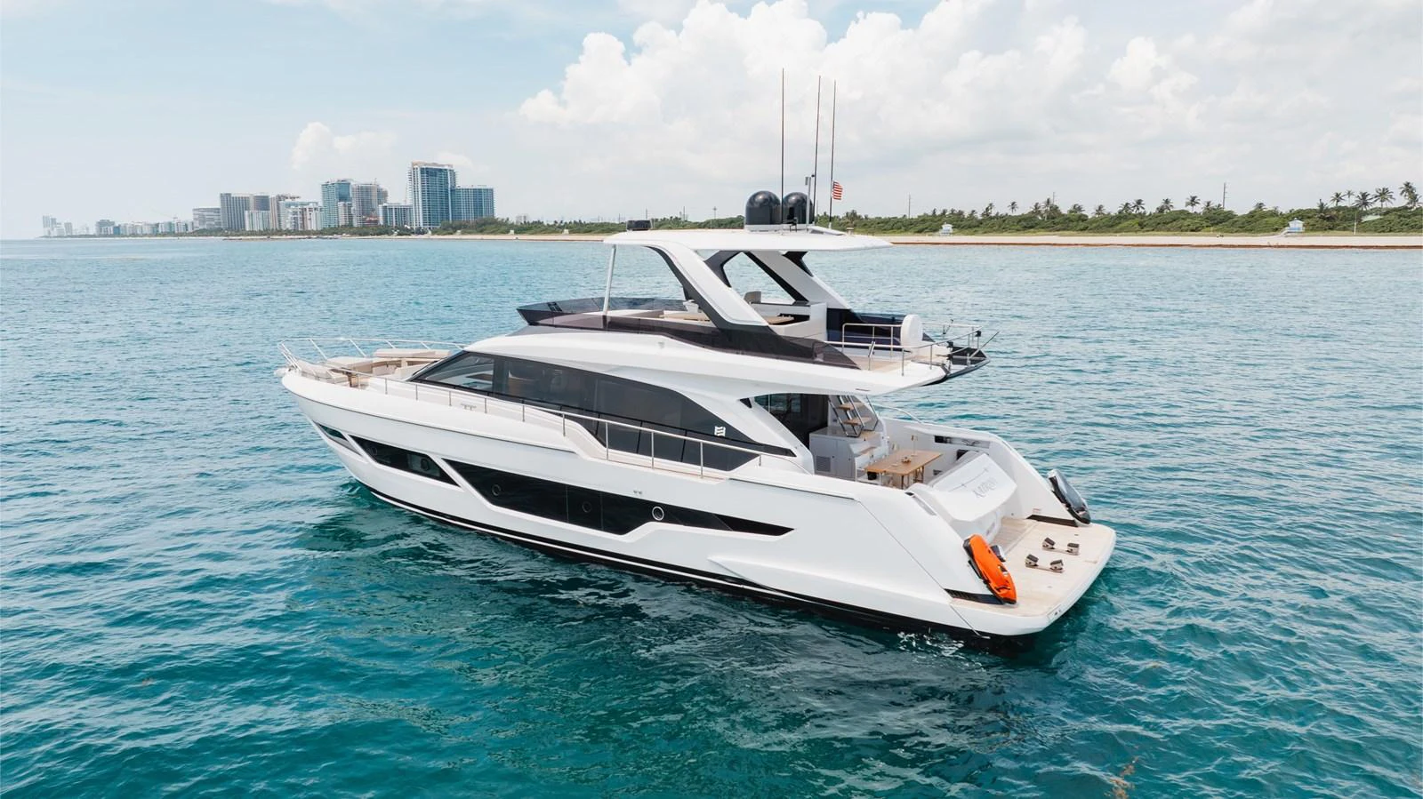 A sleek and modern yacht cruising on calm blue waters with a cityscape in the background. aboard KATRIN I Yacht for Sale