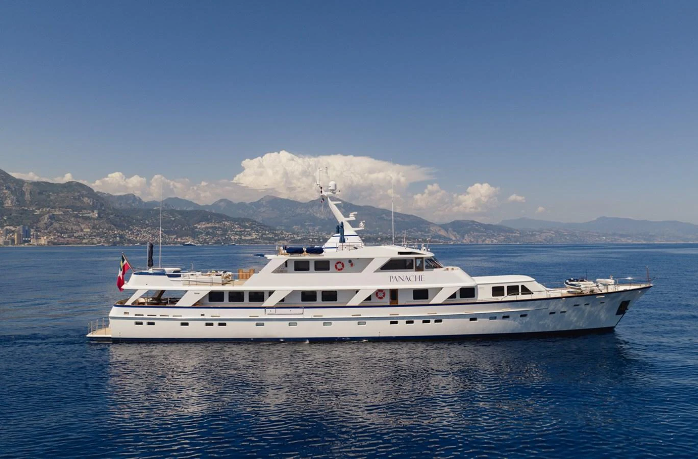 A classic motor yacht cruising on calm blue waters with a scenic coastal backdrop. aboard PANACHE Yacht for Sale