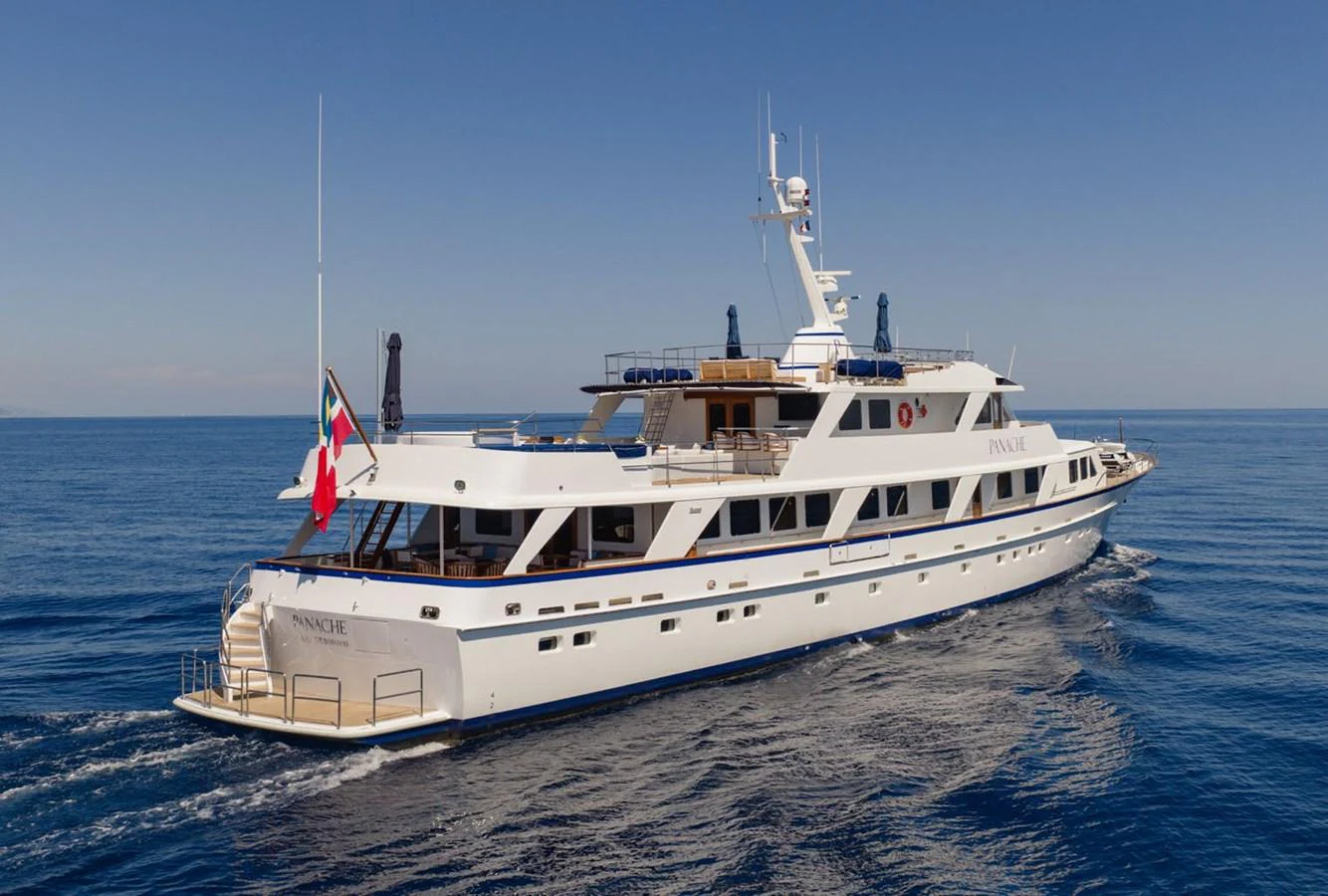 A luxurious yacht cruising smoothly on a clear, calm sea under a bright blue sky. aboard PANACHE Yacht for Sale