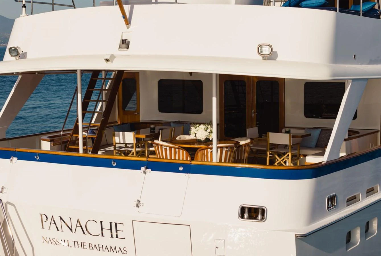 The aft deck of this yacht features a cozy outdoor dining area with elegant wooden chairs and a table set for a meal. aboard PANACHE Yacht for Sale