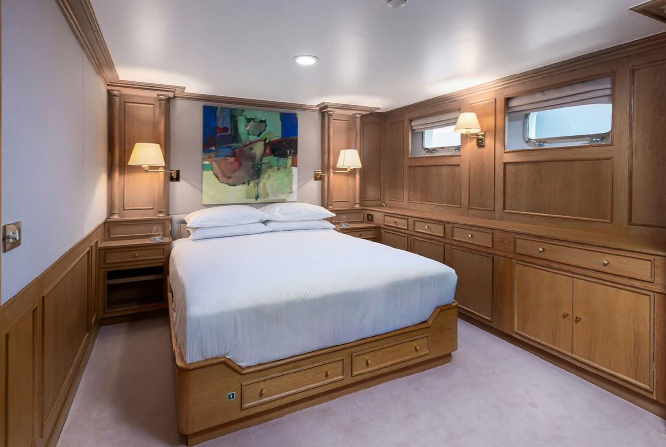 The stateroom features a cozy bed with elegant wooden paneling and soft lighting. aboard PANACHE Yacht for Sale