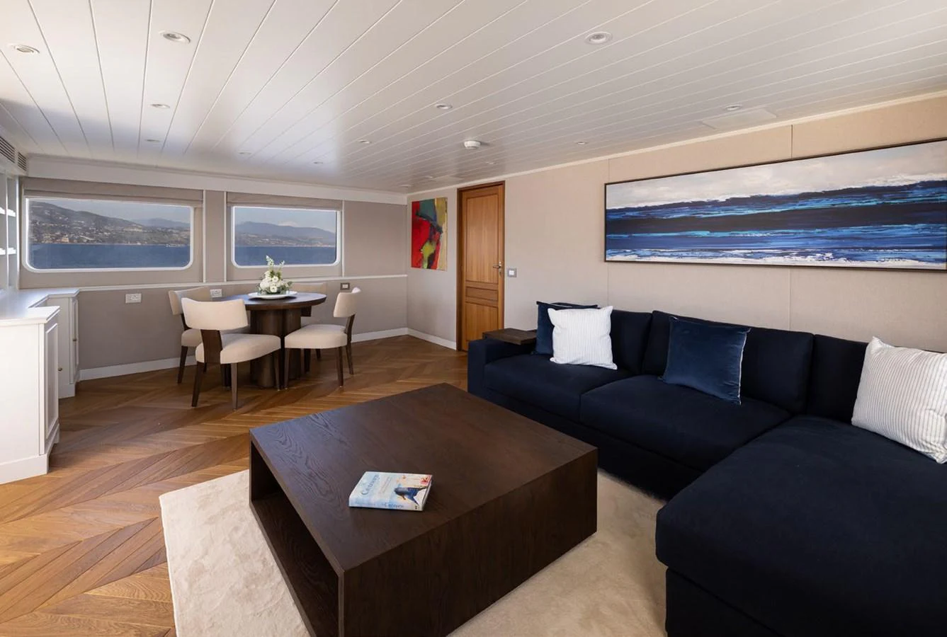 The salon features a spacious seating area with a large sectional sofa and a modern dining table, offering panoramic views through large windows. aboard PANACHE Yacht for Sale