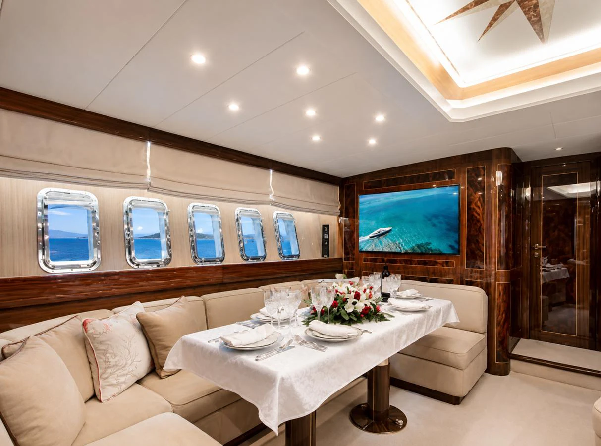 The yacht's dining area features an elegant table setting with plush seating and a view of the sea through multiple portholes. aboard ANGELINA Yacht for Sale