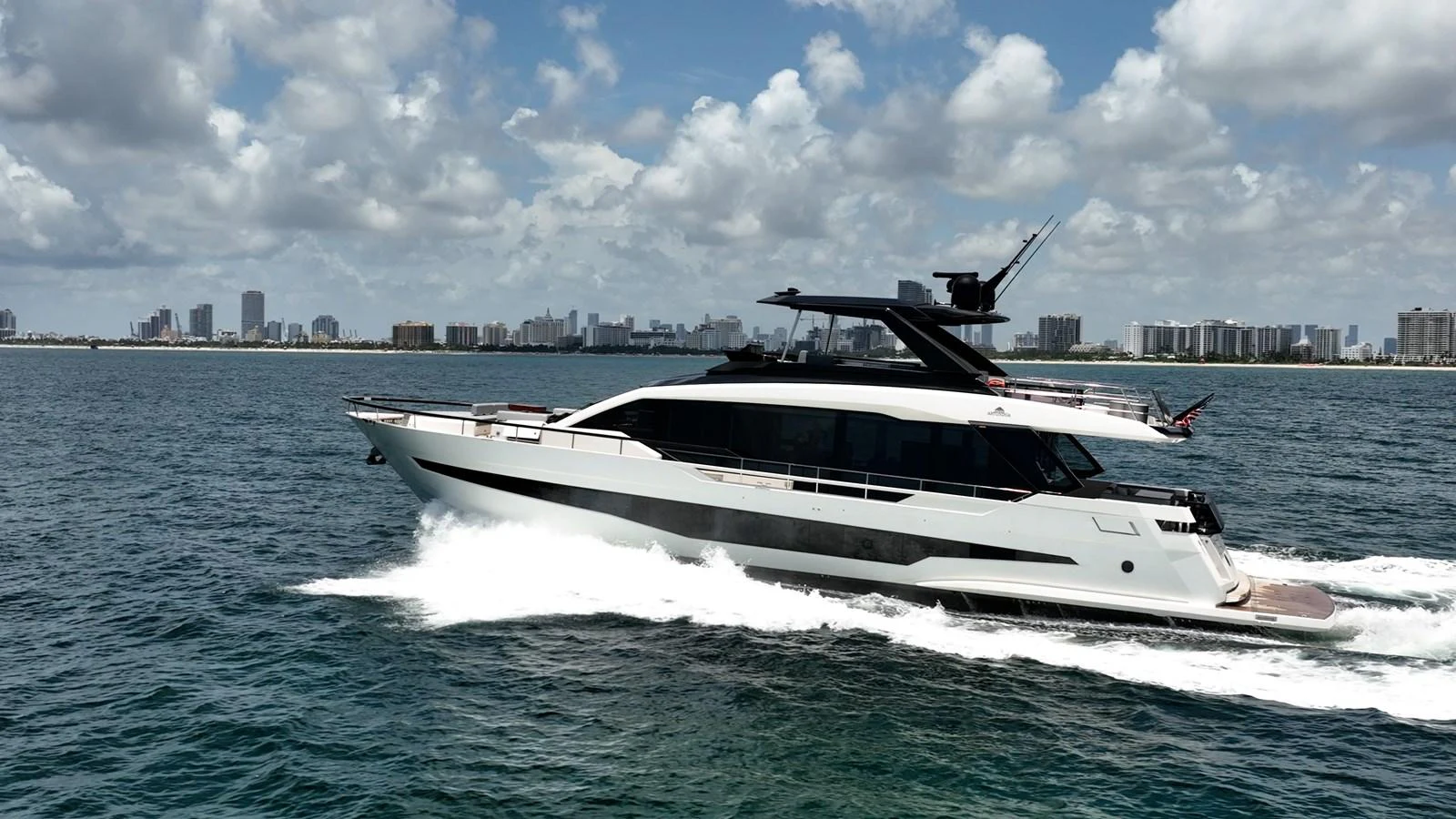 A sleek and modern yacht cruises through the water with a city skyline in the background. aboard HOTEL COLLECTION Yacht for Sale