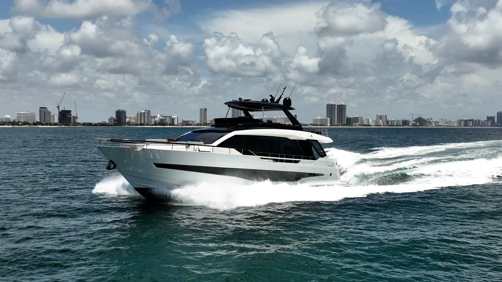 A sleek yacht cruises swiftly through the water with a cityscape in the background. aboard HOTEL COLLECTION Yacht for Sale