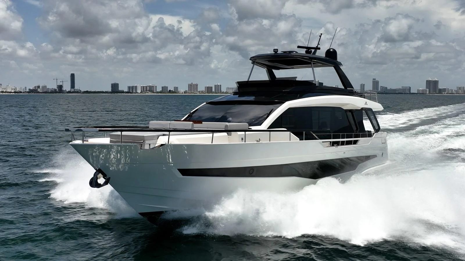 A sleek yacht cruises swiftly through the water with a city skyline in the background. aboard HOTEL COLLECTION Yacht for Sale