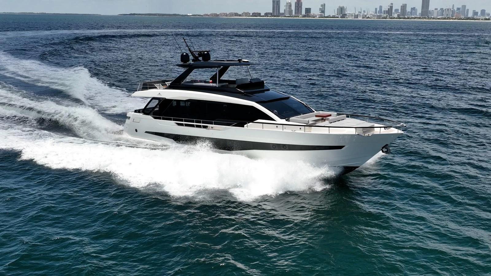 A sleek, modern yacht cruises swiftly through the open water with a cityscape in the background. aboard HOTEL COLLECTION Yacht for Sale