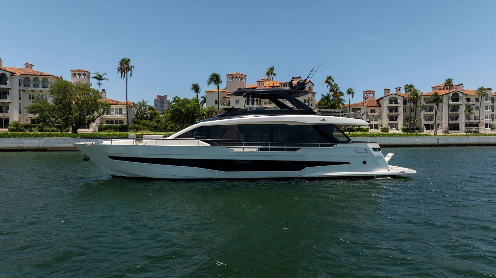 A sleek and modern yacht cruising along a picturesque waterfront with luxurious residences in the background. aboard HOTEL COLLECTION Yacht for Sale