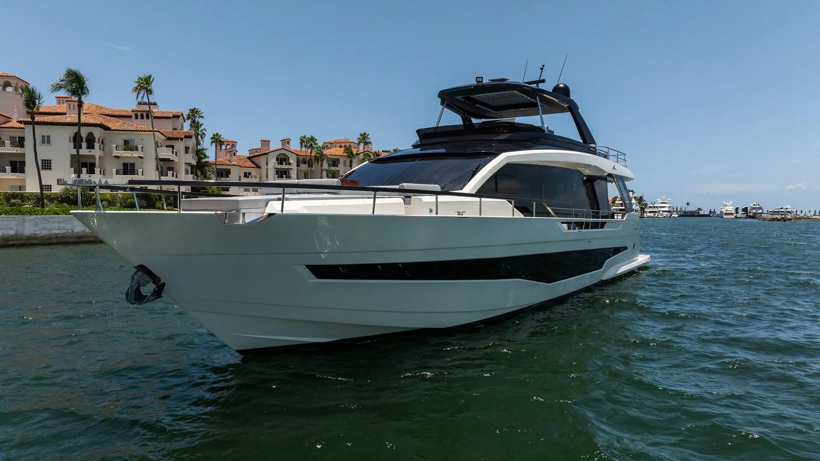 A sleek and modern yacht cruising near a picturesque waterfront with luxury residences in the background. aboard HOTEL COLLECTION Yacht for Sale