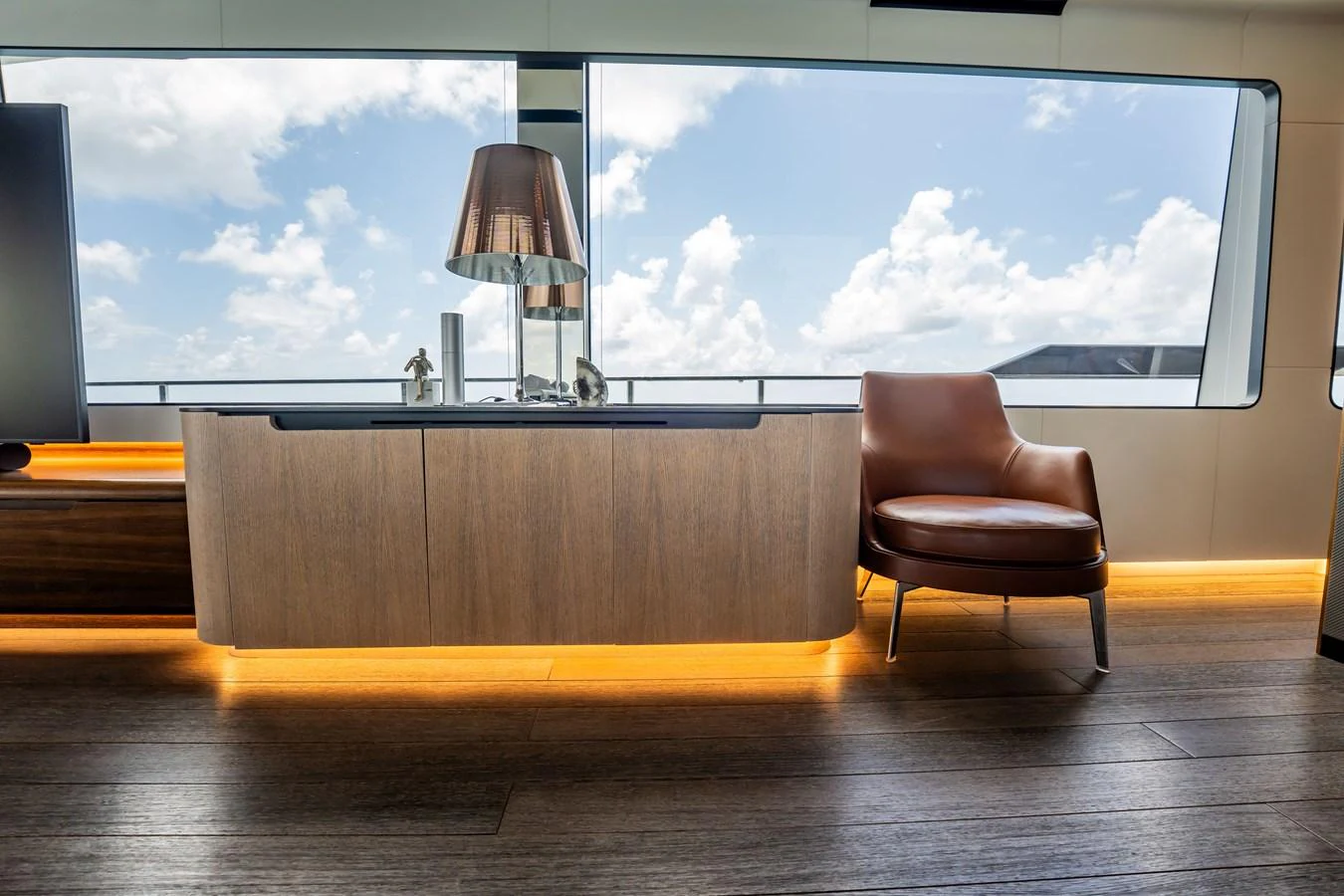 A modern interior space with a sleek cabinet and a comfortable leather chair, illuminated by natural light. aboard HOTEL COLLECTION Yacht for Sale