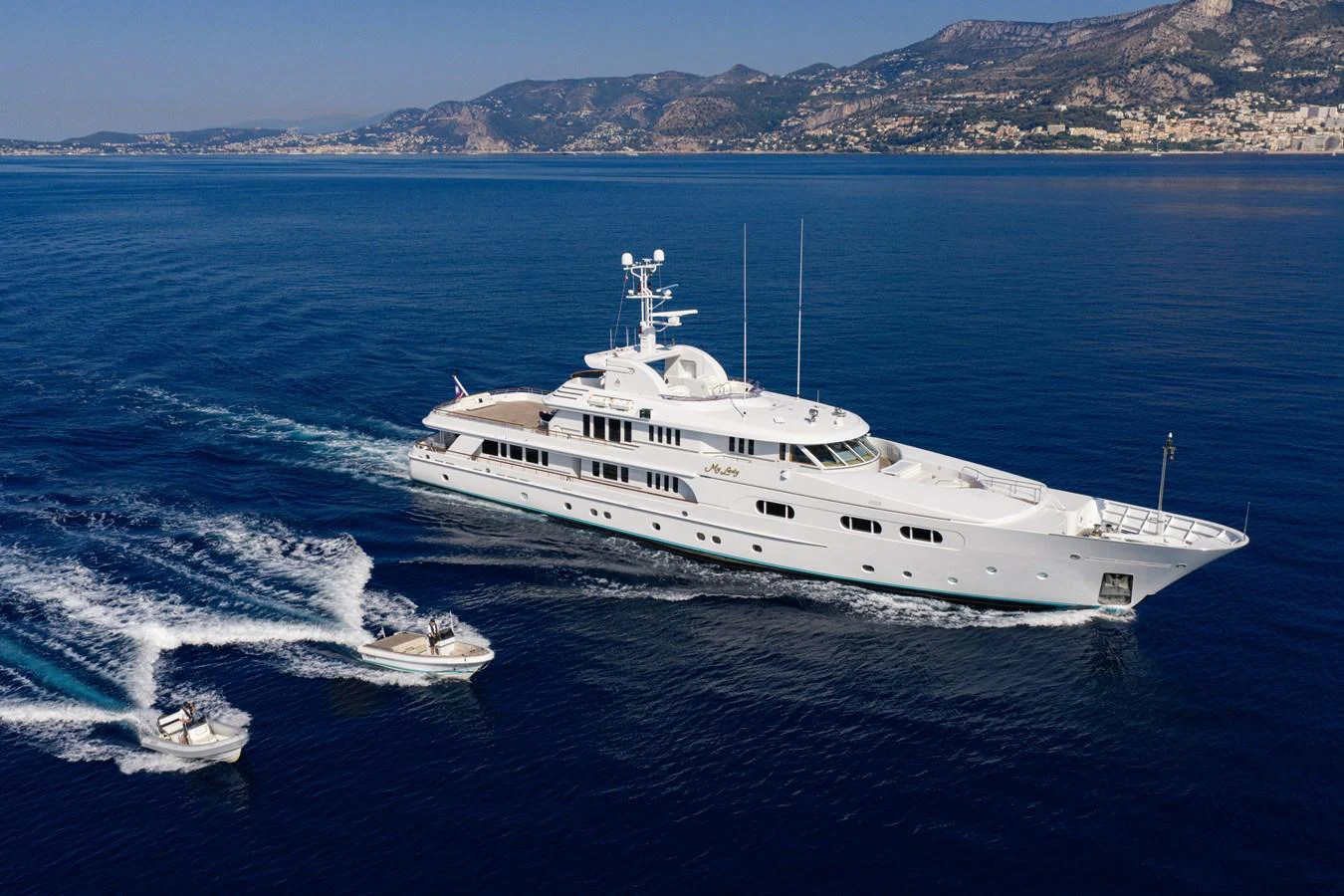 A luxurious yacht cruises through serene blue waters, accompanied by two tenders. aboard MY LADY Yacht for Sale