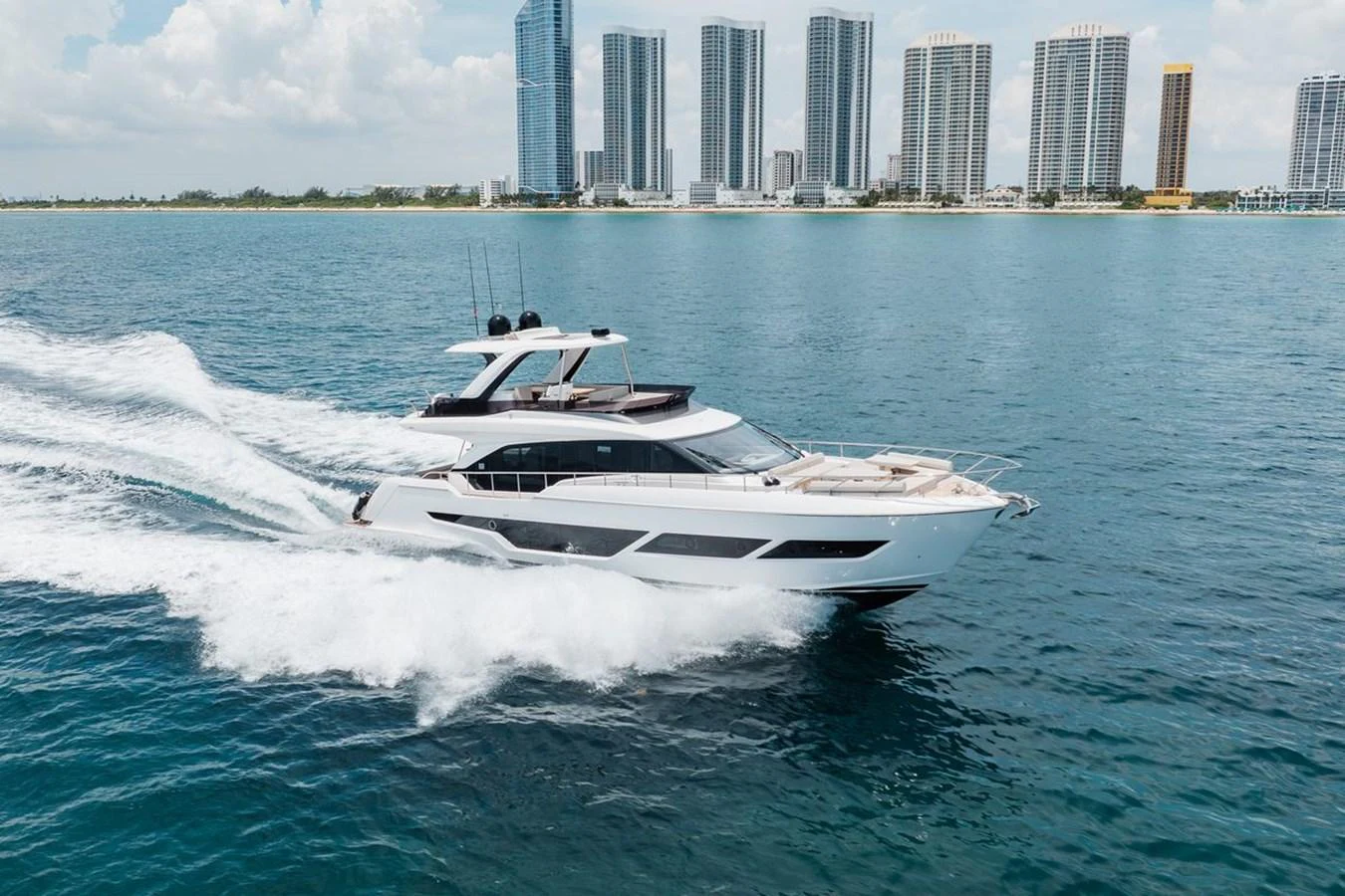 A sleek yacht cruises swiftly through the water with a city skyline in the background. aboard 2025 FERRETTI 670 KATRIN I Yacht for Sale