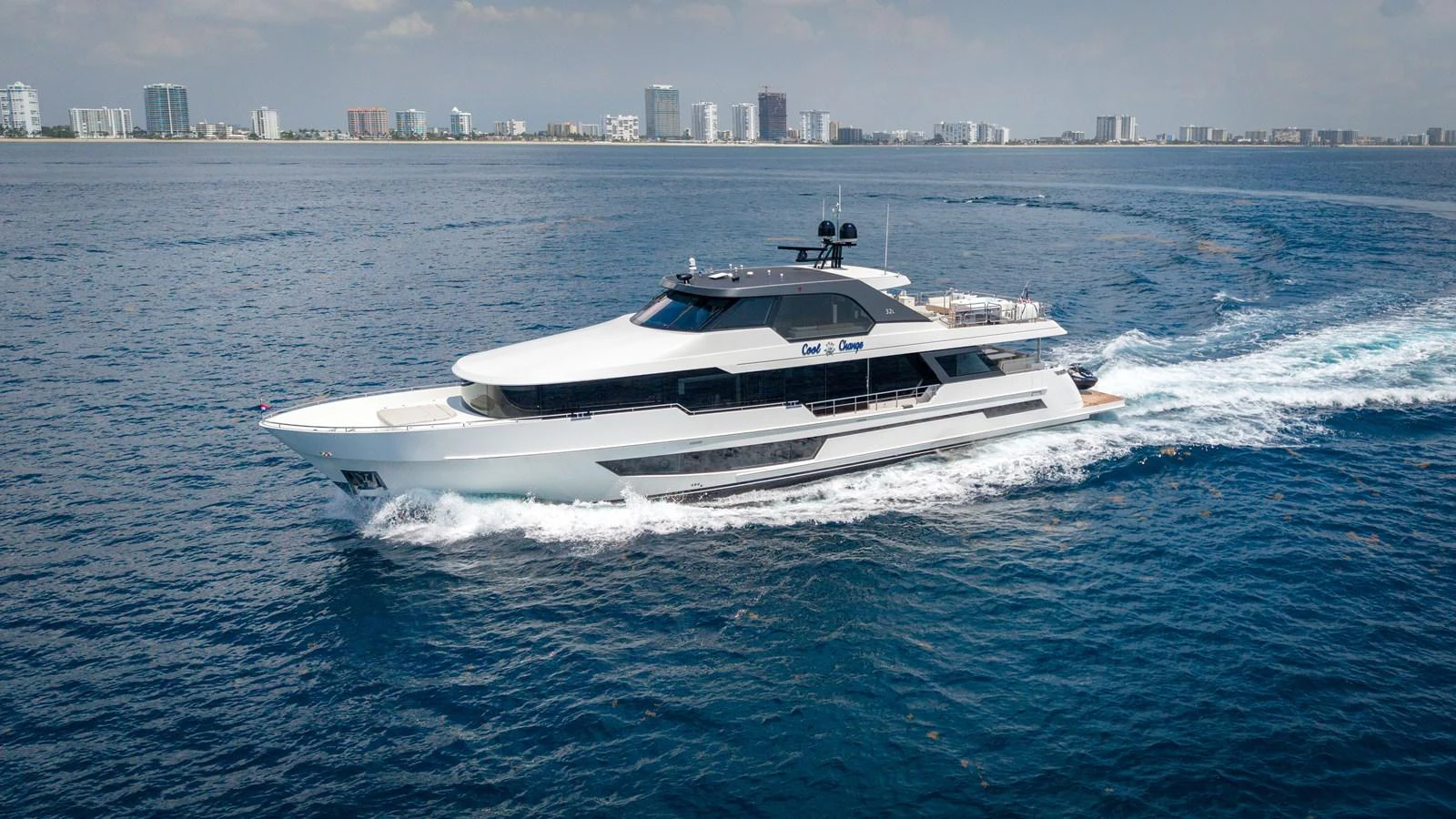 A sleek and modern yacht cruises through the open water with a cityscape in the background. aboard COOL CHANGE Yacht for Sale