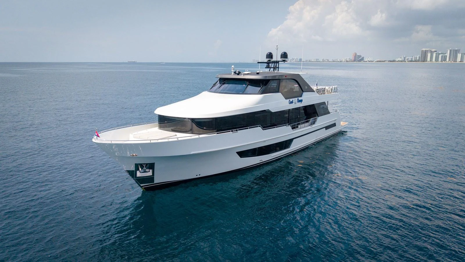 A sleek and modern yacht cruising on calm waters with a cityscape in the background. aboard COOL CHANGE Yacht for Sale
