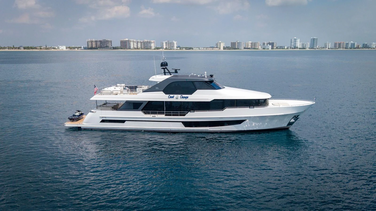 A sleek and modern yacht cruising on calm waters with a cityscape in the background. aboard COOL CHANGE Yacht for Sale