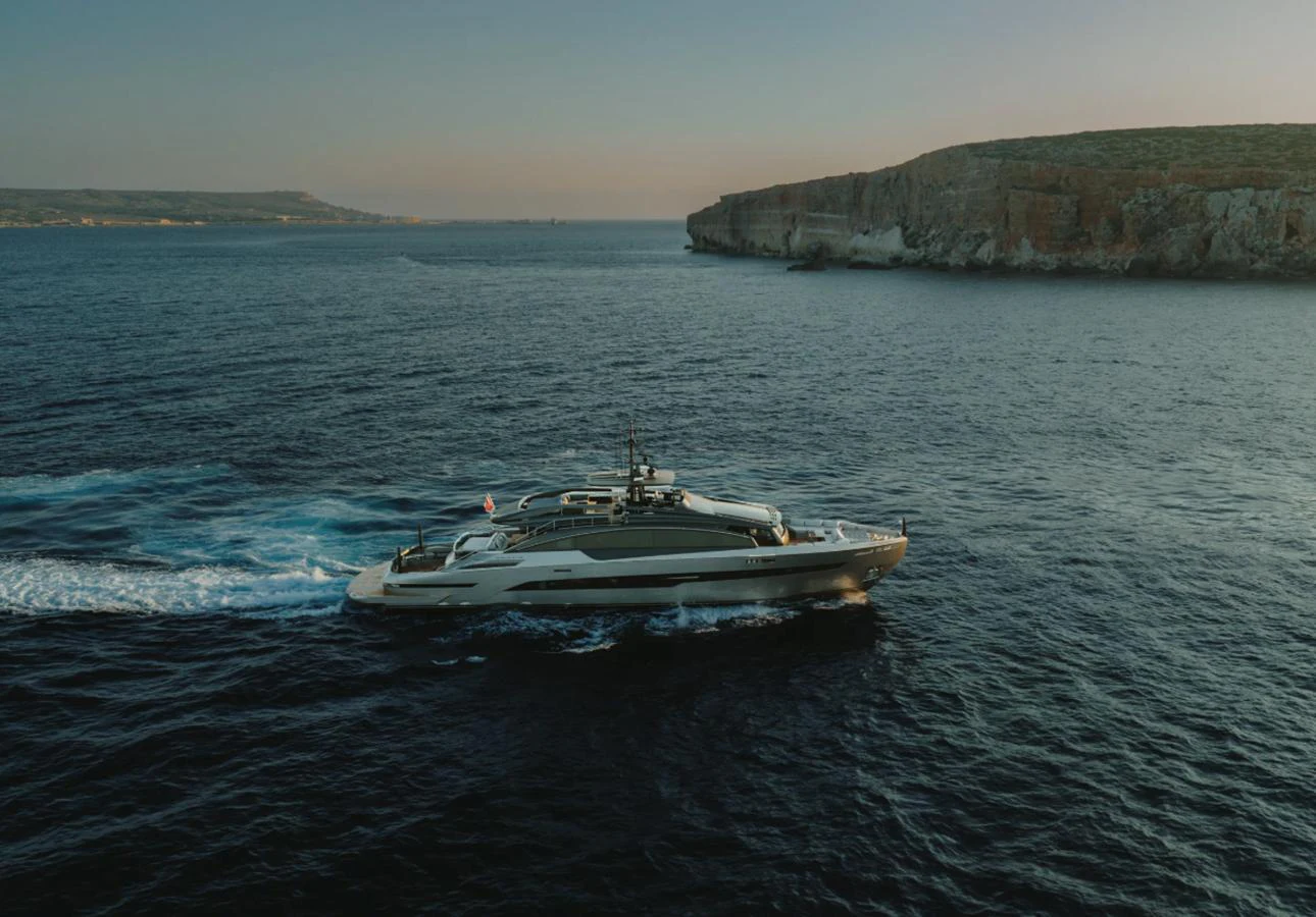 A sleek yacht cruises through calm waters with a scenic cliffside in the background. aboard BYEEE... Yacht for Sale
