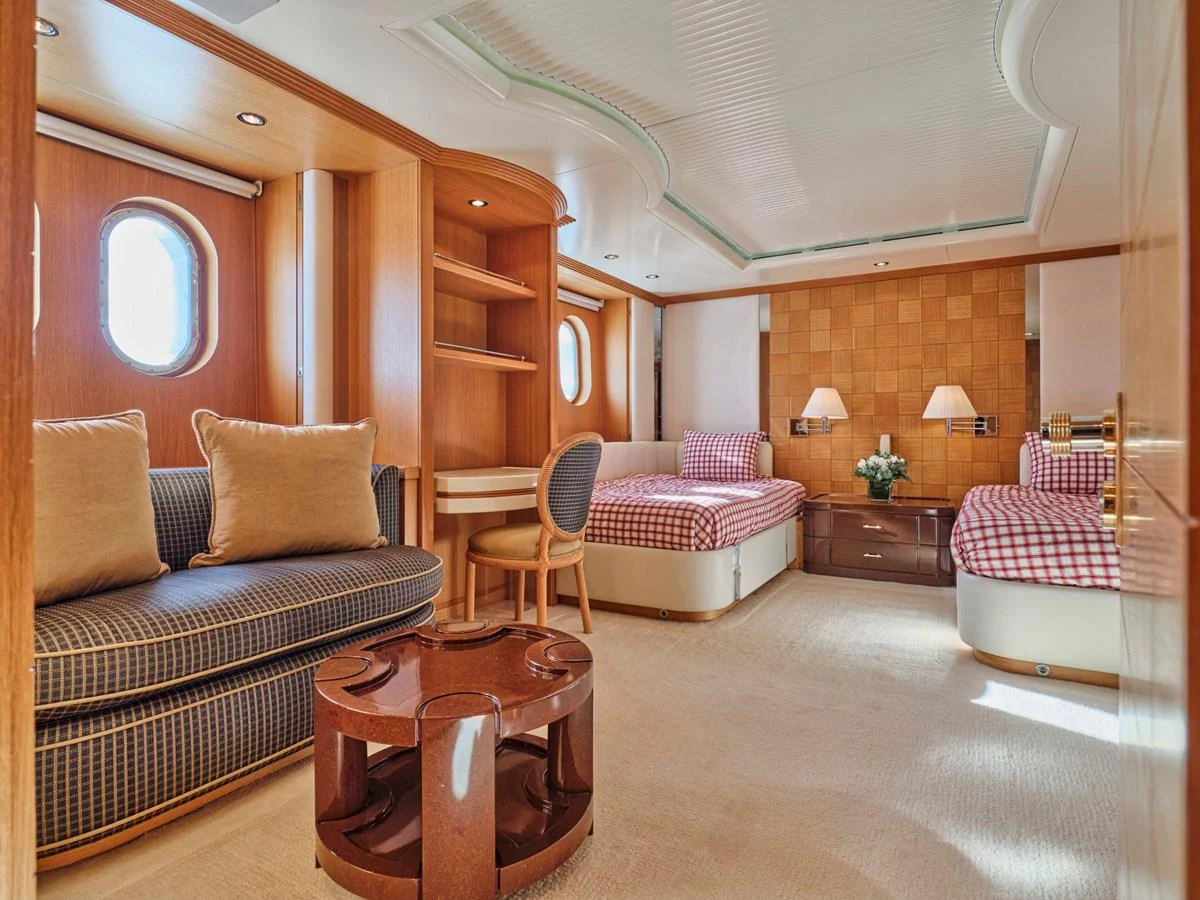 A cozy guest stateroom featuring twin beds, a seating area, and warm wooden accents. aboard SAHAB IV Yacht for Sale