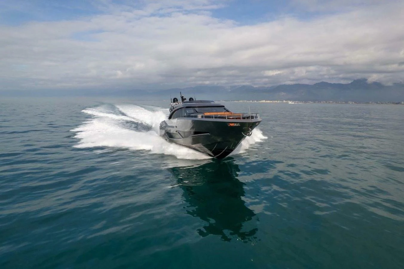 A sleek, dark-colored yacht cruises swiftly across calm waters under a partly cloudy sky. aboard AB 100/05 Yacht for Sale