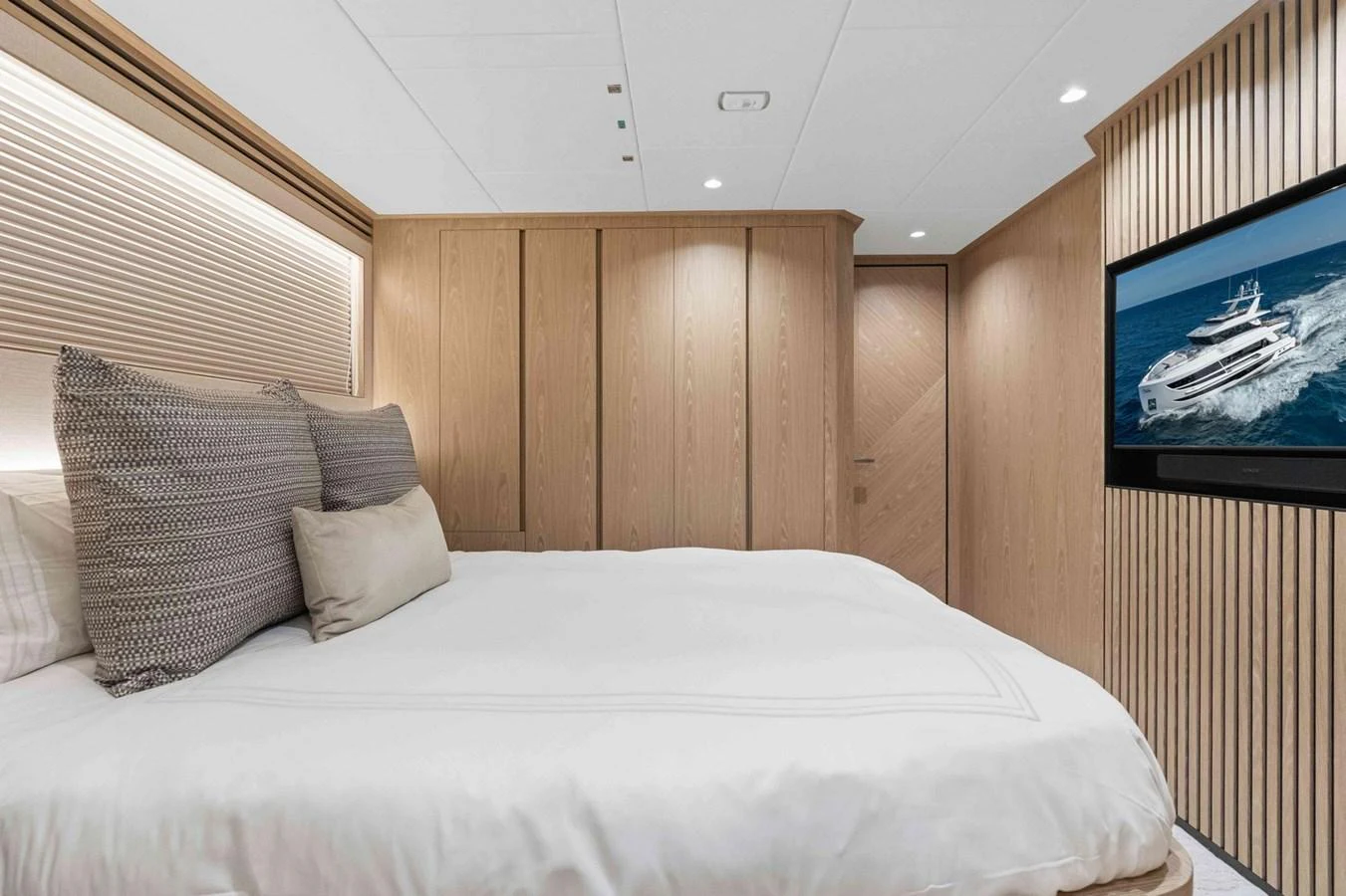 The stateroom features a luxurious bed with plush pillows and a large TV screen. aboard THE ROCK Yacht for Sale