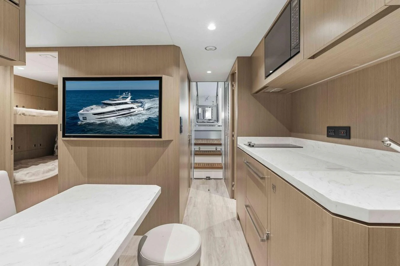 The yacht's interior features a modern galley and dining area with sleek wooden cabinetry and a large TV screen. aboard THE ROCK Yacht for Sale