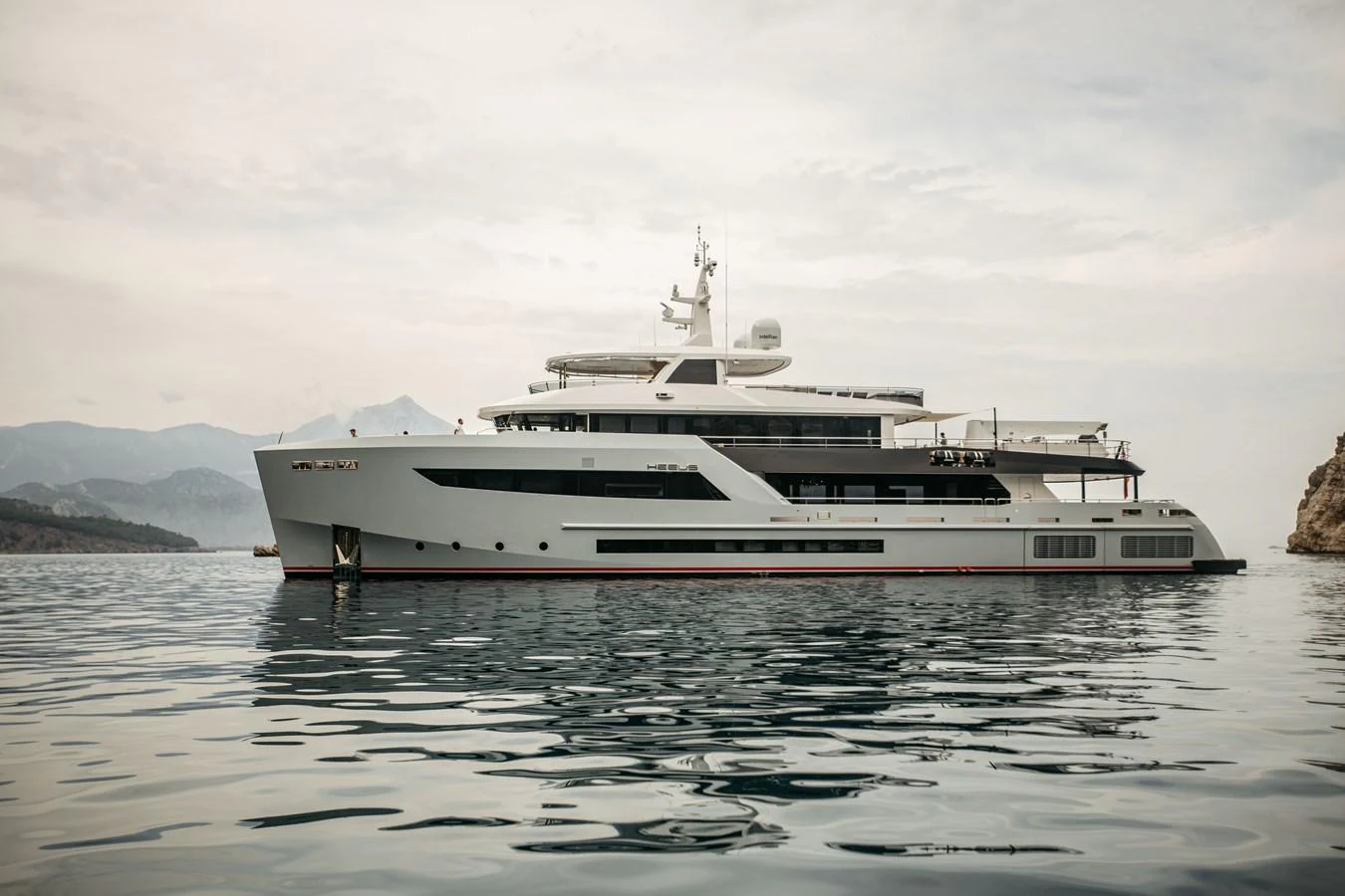 A sleek and modern yacht glides gracefully on calm waters with a mountainous backdrop. aboard BERING 145 Yacht for Sale