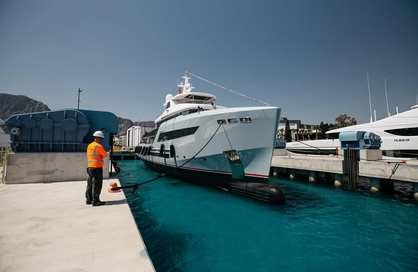 A sleek yacht is docked at a marina, with a crew member attending to the mooring lines. aboard BERING 145 Yacht for Sale