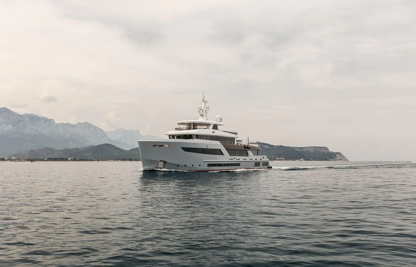 A sleek yacht cruises gracefully on calm waters with a mountainous backdrop. aboard BERING 145 Yacht for Sale