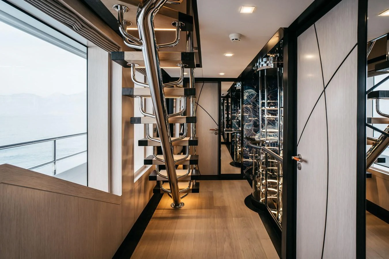 A modern interior hallway featuring a sleek spiral staircase and large windows with ocean views. aboard BERING 145 Yacht for Sale