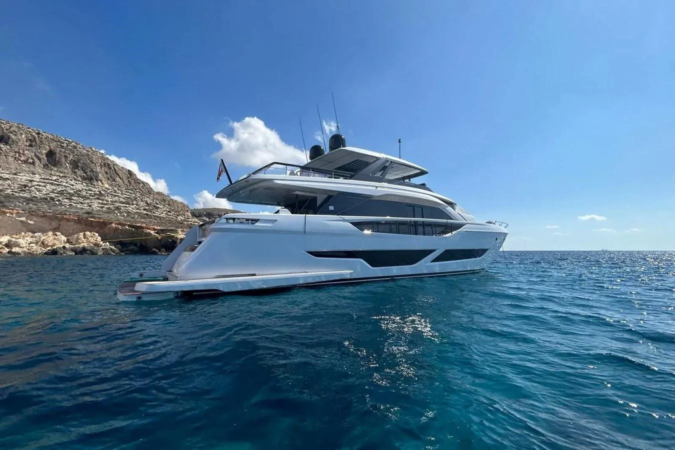 A sleek and modern yacht cruising on clear blue waters with a rocky coastline in the background. aboard SAVIENNE Yacht for Sale